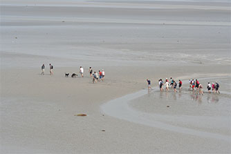 groupe de touristes traversant la Baie du Mont Saint-Michel à pied à marée basse 