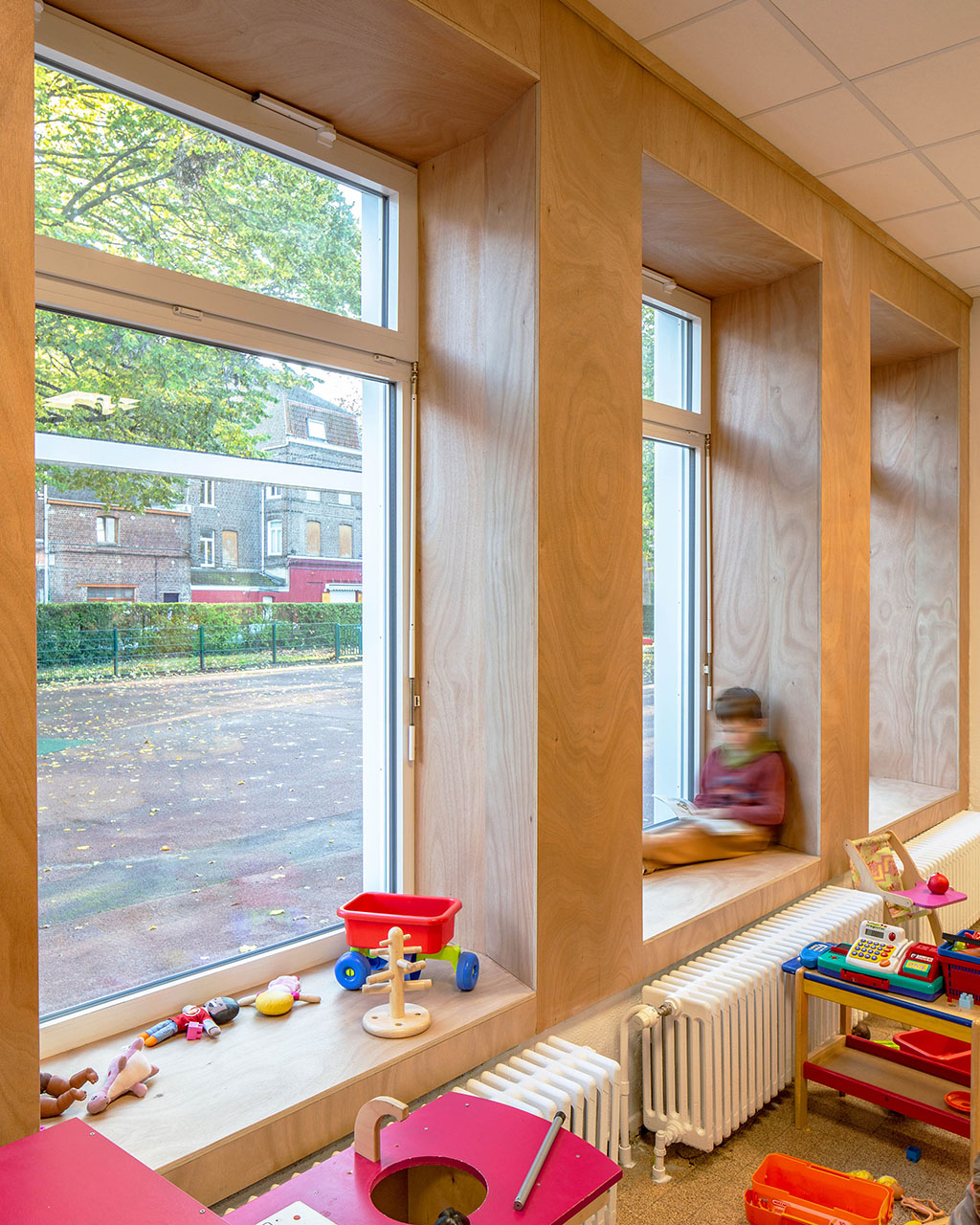 Un enfant lit un livre au bord de la fenêtre, dans une salle de classe récemment rénovée.