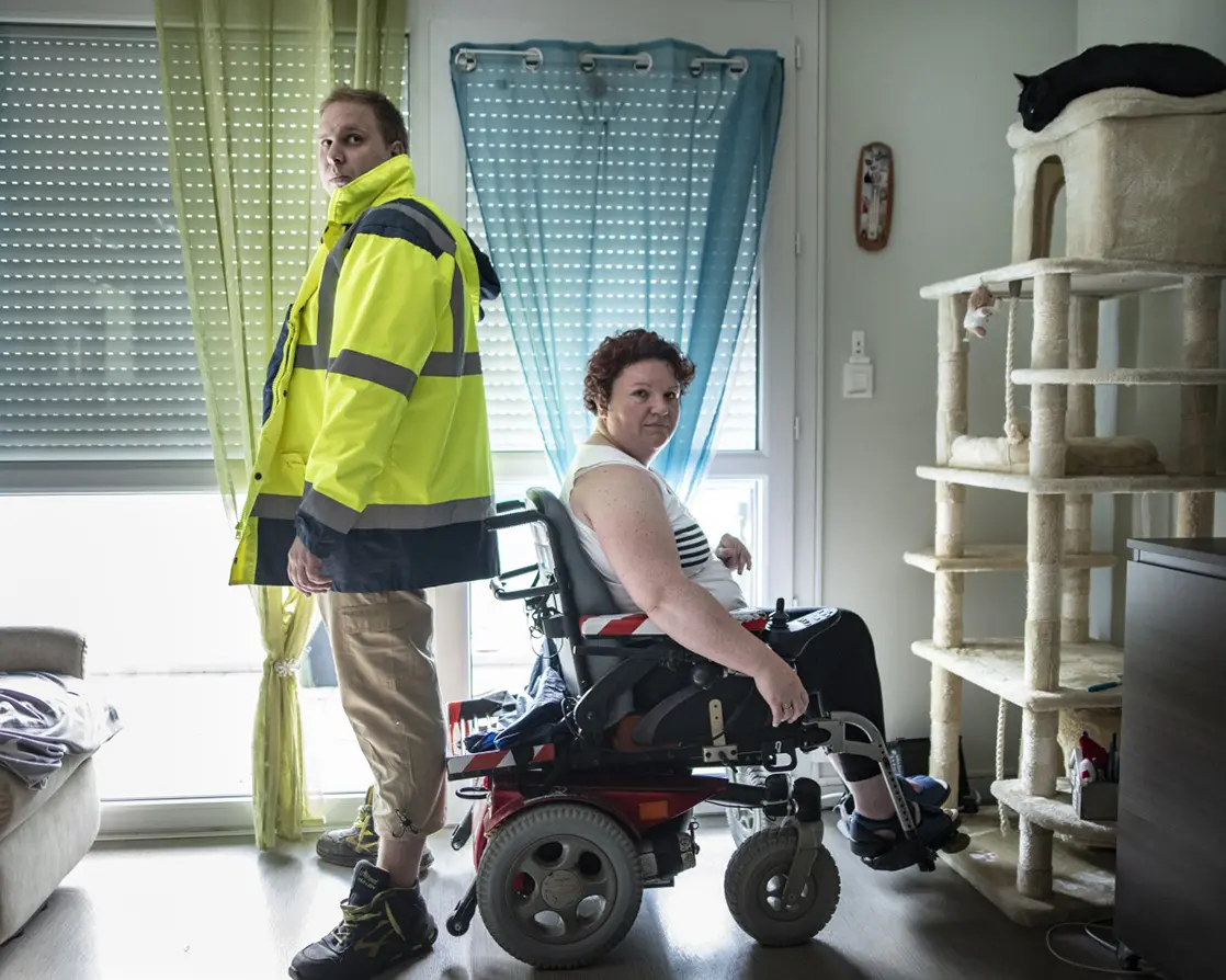 couple composé d'un homme debout portant un gilet jaune de travail et d'une femme en fauteuil roulant chez eux