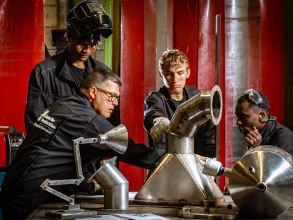 De jeunes apprentis et leur formateur sont en tenue de travail dans un atelier de chaudronnerie.