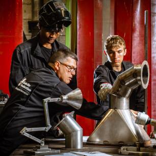 De jeunes apprentis et leur formateur sont en tenue de travail dans un atelier de chaudronnerie.